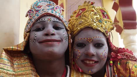 Handheld-closeup-of-two-young-girls-in-an-Indian-town-dressed-as-Goddess-for-alms-and-celebrations-divinity-and-bless-tourists-look-at-camera-and-smile