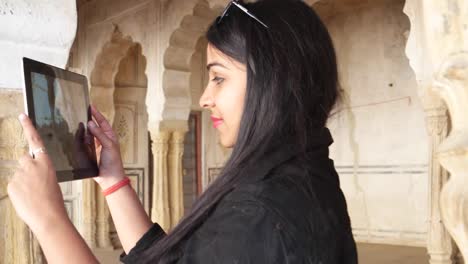 Beautiful-woman-with-black-eyes-taking-photos-and-working-on-a-touch-screen-tablet-pad-handheld-business-network-online-wireless-connection-at-an-old-building-complex-ancient-Indian-temple-column