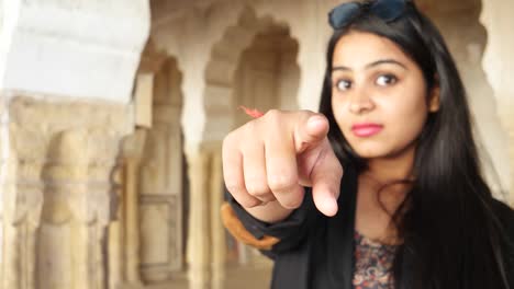 Young-beautiful--Indian-woman-looking-at-camera-and-pointing-finger-straight-at-camera-order-punish-select-at-an-interior-of-an-Indian-temple-old-building-interior-in-Rajasthan-handheld-closeup