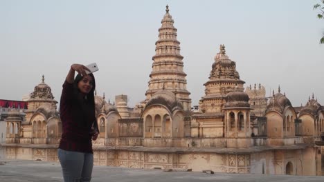 Woman-in-front-of-panoramic-attractive-ornate-temple-fort-palace-complex-from-a-vantage-point-higher-level-taking-selfie-photo-on-mobile-phone-camera-tourist--Hindu-religious-massive-love-handheld-pov