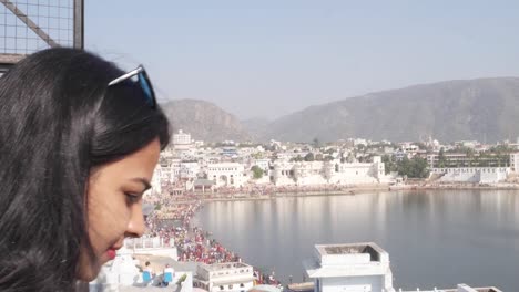 Handheld-Frau-nimmt-Selfie-Foto-Video-mit-ihrem-mobilen-Handy-Gerät-von-einem-Panorama-Aussichtspunkt-Blick-des-Heiligen-Pushkar-See,-eine-heilige-Stadt-für-Hindu-Pilger-Mela-Festival-Baden-Ghats-Tempel