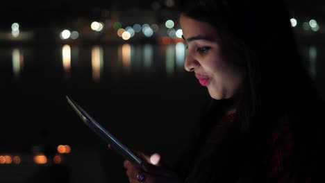 Young-woman-video-chats-talks-smiles-on-tablet-pad-waves-hands-bye-greets-welcomes-touch-screen-information-travel-network-surf-internet-points-at-the-Hindu-temple-holy-town-lake-city-handheld-con-cal