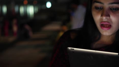 Young-woman-video-chats-talks-smiles-on-tablet-pad-waves-hands-bye-greets-welcomes-touch-screen-information-travel-network-surf-internet-points-at-the-Hindu-temple-holy-town-lake-city-handheld-con-cal