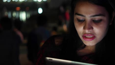 Young-woman-video-chats-talks-smiles-on-tablet-pad-waves-hands-bye-greets-welcomes-touch-screen-information-travel-network-surf-internet-points-at-the-Hindu-temple-holy-town-lake-city-handheld-con-cal