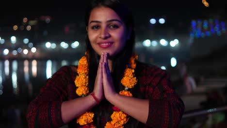 Beautiful-young-woman-hands-joined-in-namaste-greets-with-orange-marigold-flower-garland-on-her-neck-offers-prayers-worship-God-Goddess-hands-welcomes-smiles-glowing-respect-believer-religion-handheld