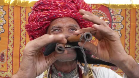 CU-Hand-held-Rajasthani-elderly-male-starts-to-play-the-flute-with-his-nose-in-front-of-a-colourful-fabric-tent