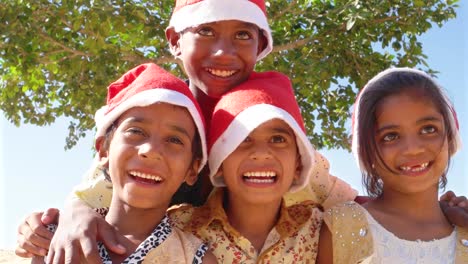 Kinder-Spaß-posiert-für-die-Kamera-mit-Santa-Hüte-mit-einem-Baum-im-Hintergrund