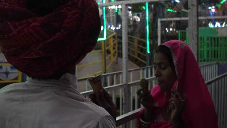 Pareja-India-comiendo-helado-en-vestidos-tradicionales-en-la-Pushkar-Mela,-un-carnaval-de-Rajasthán,-la-India