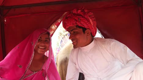 Tiro-mano-de-India-pareja-disfrutando-de-un-paseo-en-camello-en-una-caravana-en-la-Feria-de-Pushkar,-Rajasthan,-India