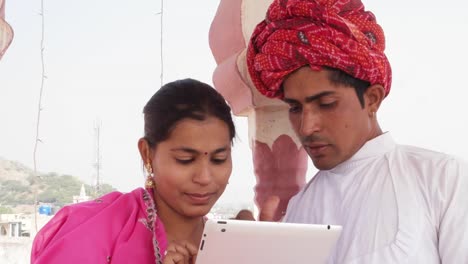 Pan-to-attractive-Indian-couple-working-learning-teaching-sharing-on-a-tablet-in-Rajasthan,-India