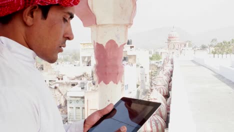 Indischer-Mann-hektisch-auf-einem-Tablet-arbeiten-und-denken-auf-einem-Hausdach-in-traditioneller-Kleidung-in-Rajasthan,-Indien