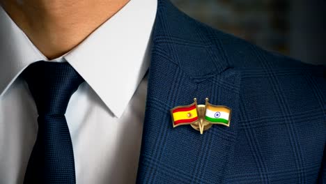 Empresario-caminando-hacia-cámara-con-amigo-país-banderas-Pin-España---India