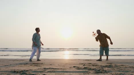 Pareja-senior-activo-jugando-a-la-pelota-de-balón-de-tai-chi-en-la-playa-a-cámara-lenta.