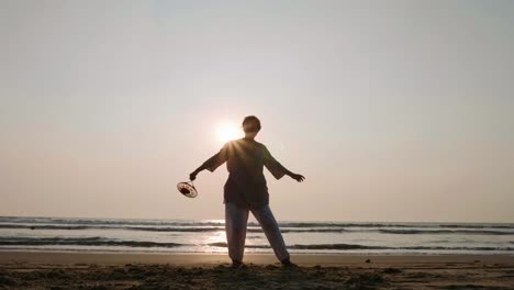 Ältere-Frau-praktizieren-Tai-Chi-Ballon-Ball-am-Strand-bei-Sonnenuntergang