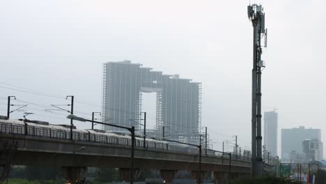 Locked-on-shot-of-a-metro-train-moving-in-front-of-skyscrapers,-Delhi,-India