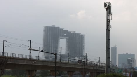 Locked-on-shot-of-a-metro-train-moving-in-front-of-skyscrapers,-Delhi,-India