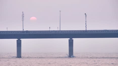 Vehicles-passing-on-a-modern-bridge-while-sun-is-setting-in-the-background