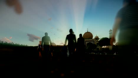 Taj-Mahal-with-tourists-walking-against-beautiful-sunset,-panning-4K