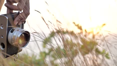 A-person-holding-a-vintage-camera-in-the-hand-and-standing-in-the-waving-grass