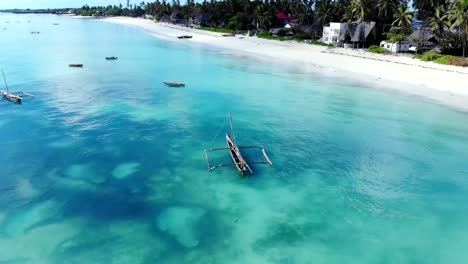 Vista-aérea-de-un-pescador-navega-en-un-barco-de-madera-en-agua-azul-clara-a-lo-largo-de-una-playa-exótica-tropical-en-África