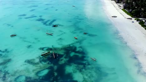 Aerial-view-of-a-fisherman-sails-on-a-wooden-boat-on-clear-blue-water-along-a-tropical-exotic-beach-in-Africa