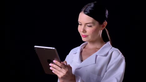 Hermosa-joven-doctora-en-blanco-capa-escribiendo-en-tableta-y-pie-aislado-sobre-fondo-negro-studio