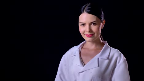 Confident-young-beautiful-woman-in-white-coat-turning-head-and-looking-at-camera,-smiling,-isolated-on-black-background