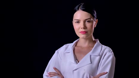 Confident-young-beautiful-female-doctor-looking-at-camera-with-crossed-hands,-standing-isolated-on-black-background