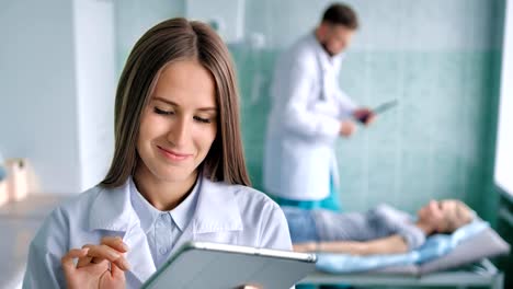 Sonriente-a-mujer-doctor-en-bata-blanca-con-paciente-preparación-de-tablet-PC-para-el-procedimiento