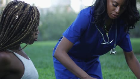 Slow-motion-of-black-nurse-stretching-another-woman's-leg-at-a-park