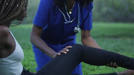 Slow-motion-close-up-of-black-nurse-stretching-another-woman's-leg-at-a-park