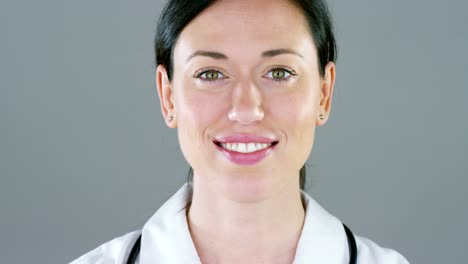 Portrait-of-a-female-doctor-with-white-coat-and-stethoscope-smiling-looking-into-camera-on-white-background.