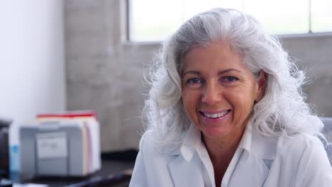 Senior-female-doctor-sitting-at-desk-in-an-office,close-up