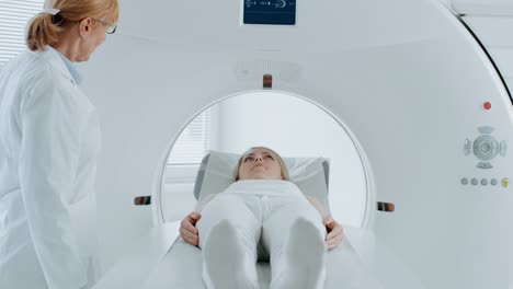 In-the-Medical-Laboratory-Female-Patient-Lying-on-a-CT-or-MRI-Scan-Bed-Undergoes-Scanning-Procedure-Under-Supervision-of-Professional-Radiologist.-Patient-Moves-Through-the-Machine-While-it-Scans.