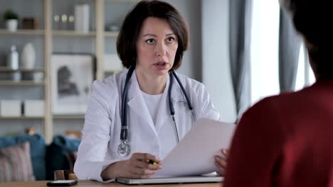 Old-Lady-Doctor-Discussing-Treatment-with-Patient-in-Clinic