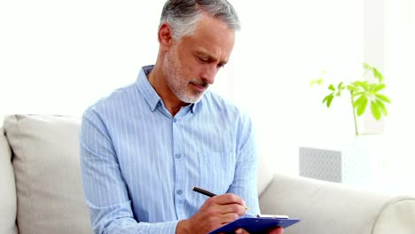 Portrait-of-a-smiling-doctor-writing-notes-on-his-clipboard