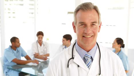 Happy-doctor-looking-at-camera-and-his-staff-behind-him