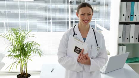 Doctor-leaning-on-desk-smiling-at-camera