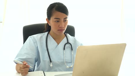 Asian-doctor-analyzing-medical-results-at-computer-and-taking-notes