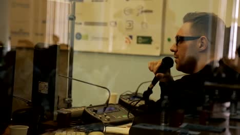 Man-with-glasses-and-a-light-stubble-holds-microphone-and-speaks-into-it-sitting-at-a-table