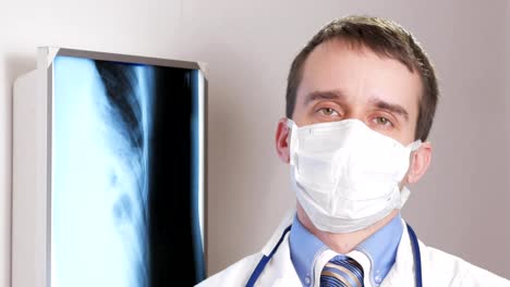 Un-joven-médico-en-una-mascarilla-mira-la-cámara-y-sonríe.-Contra-el-fondo-colgante-radiografía-del-paciente.-Camisa-con-una-corbata-y-un-estetoscopio-en-el-cuello