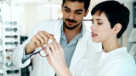 Beautiful-woman-with-optician-trying-eyeglasses-at-optics-store