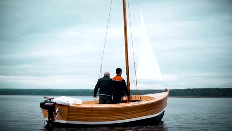 Wood-sailboat-with-two-men-trying-to-set-mast