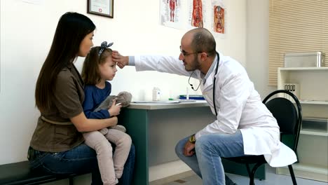 Male-pediatrician-checking-little-girl-head-temperature-with-his-hand-and-giving-her-thermometer