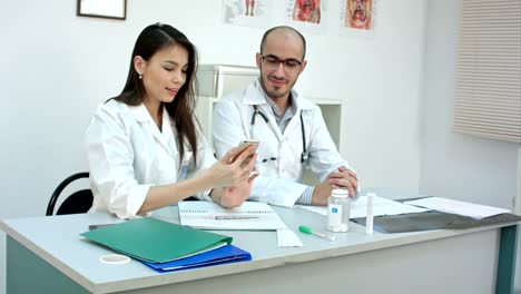 Médico-joven-y-guapa-enfermera-tomar-autorretratos-en-el-teléfono-en-su-escritorio