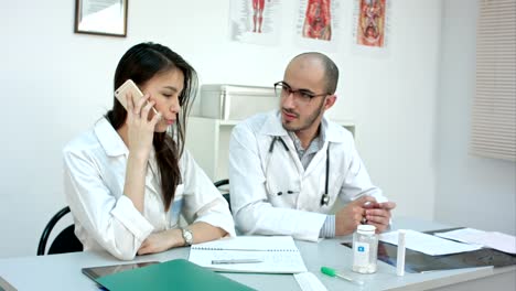 Female-doctor-talking-on-the-phone-asking-her-male-coworker-for-advice