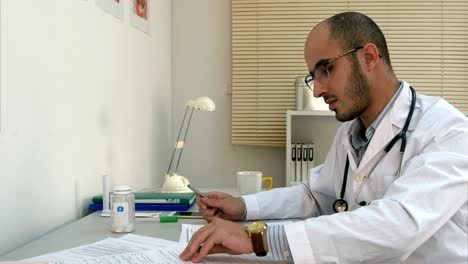 Busy-male-physician-working-with-papers-and-having-phone-conversation-in-his-office