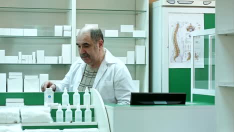Senior-männlichen-Apotheker-mit-Schnurrbart-posiert-in-der-Apotheke,-arbeiten-mit-Medizin-und-computer