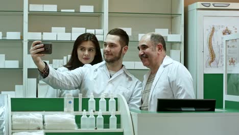 Equipo-alegre-de-farmacéutico-y-pasantes-tomar-selfie-vía-smartphone-en-el-lugar-de-trabajo