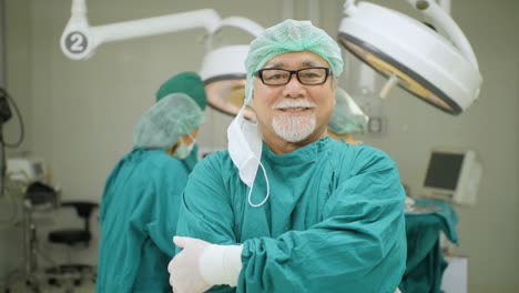 Porträt-von-senior-männlichen-Chirurg-tragen-volle-chirurgische-scheuert-sich-lächelnd-Kamera-mit-auf-Patienten-im-Operationssaal-im-Krankenhaus-tätigen-Ärzte.